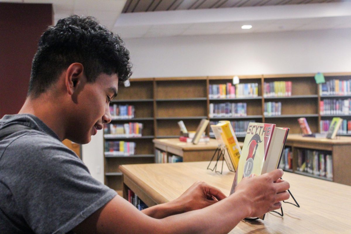 Eddy Nolasco Alvarez, junior, looks at the book Scythe by Neal Shusterman in Lawrence Centrals brand new library